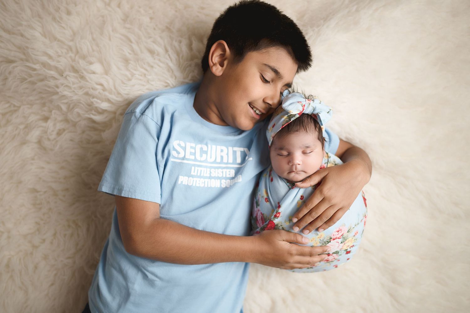 Newborn photography session showing baby swaddled in white fabric on light background with sibling interaction.