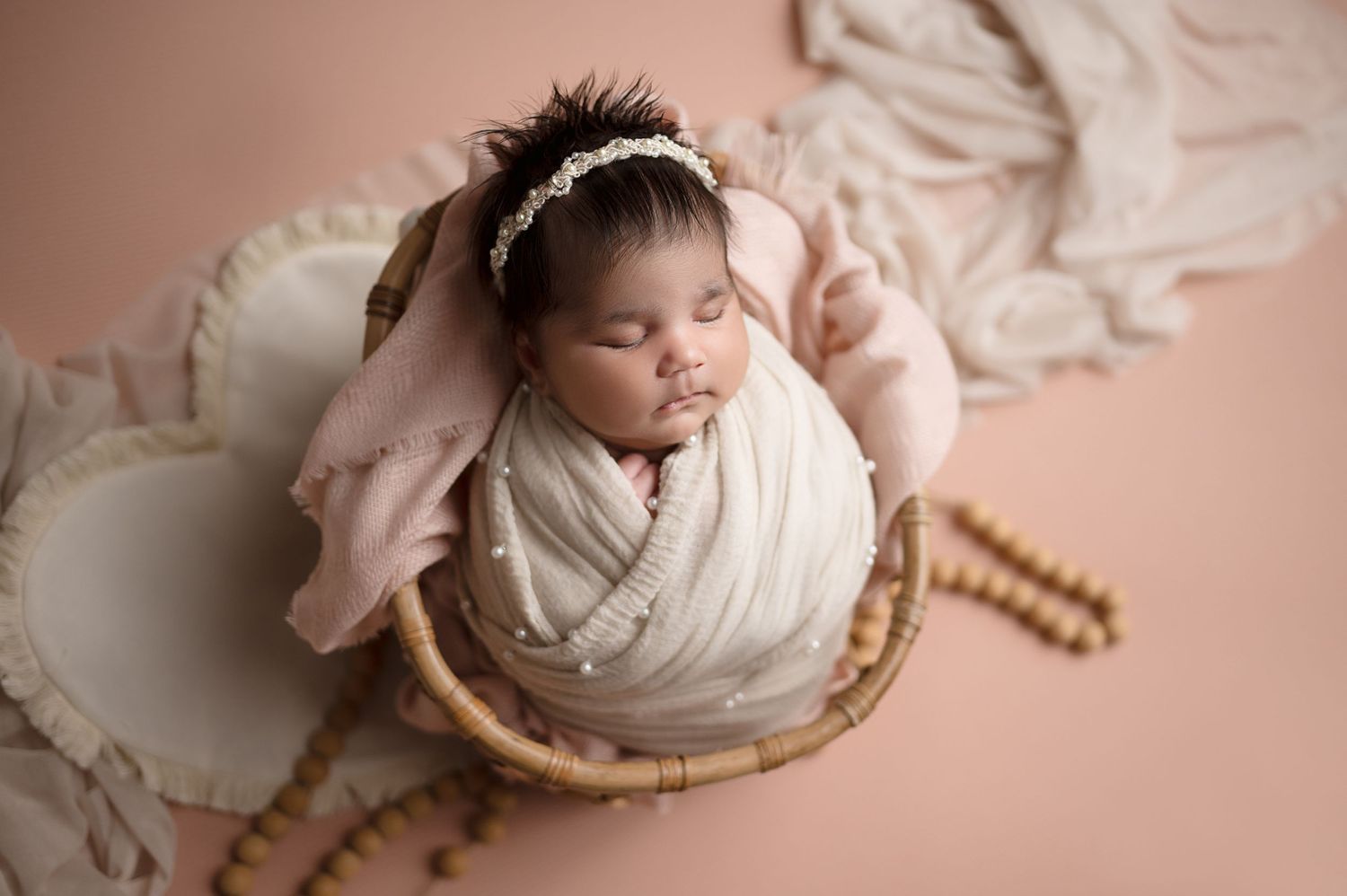 Sleeping newborn wrapped in pink swaddle lying in decorative basket.