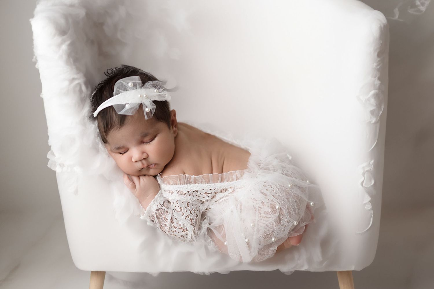 Artistic newborn portrait on white fluffy backdrop with lace accents.