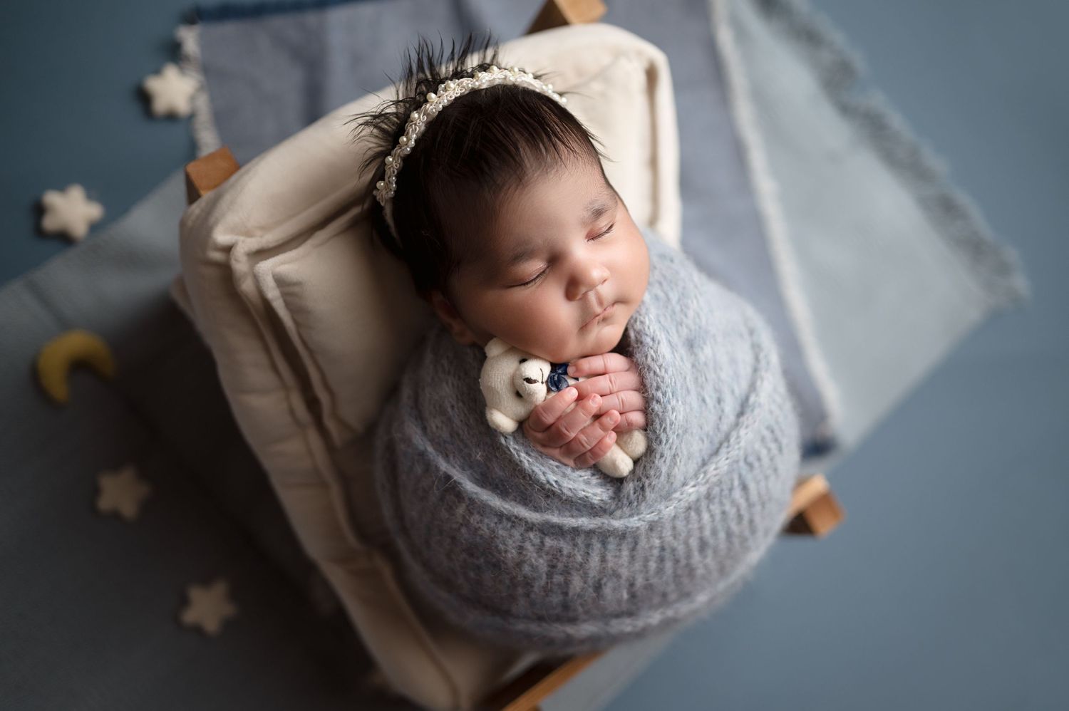 Artistic newborn photo with grey wrap and star decorations in muted tones.