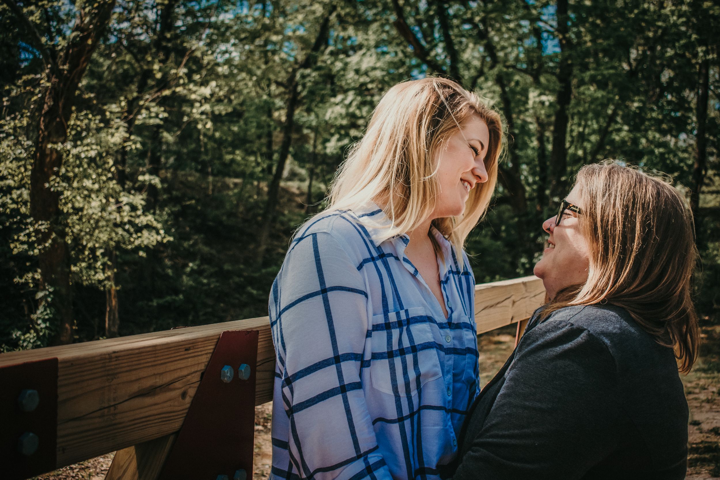 A beautiful queer couple poses on a bridge, looking into each others eyes with love