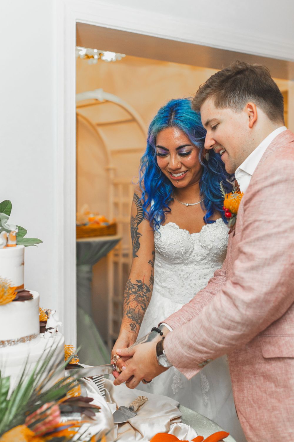 Couple cutting their wedding cake together with bride in white dress and groom in pink suit.