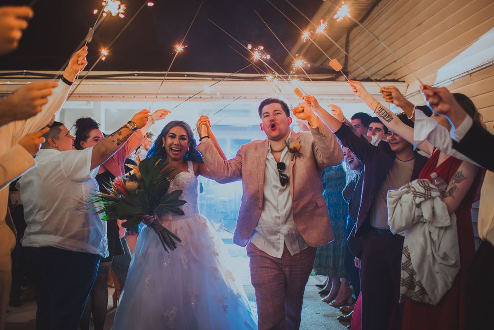 Wedding couple exits under sparkler arch surrounded by celebrating guests.