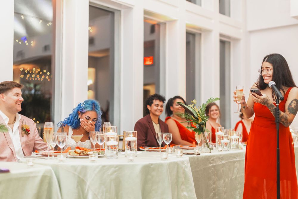 Wedding reception dinner with guests seated at decorated tables while someone gives a speech.