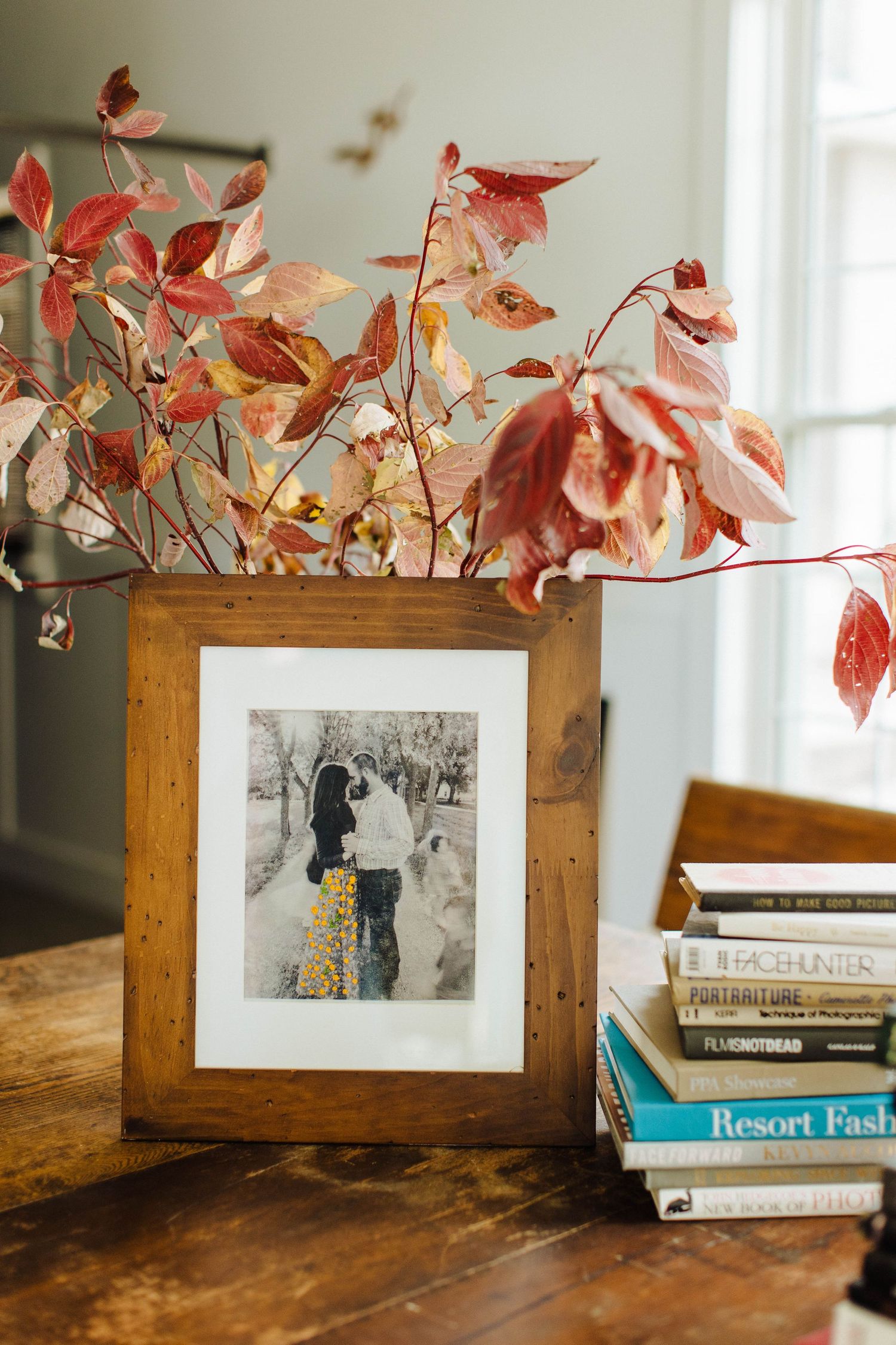 Framed vintage photographs displayed on wooden surface with autumn leaves and books.