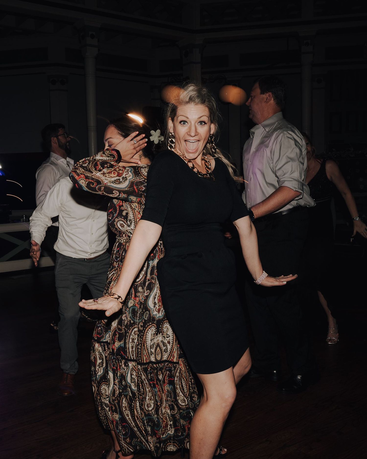 Guests dancing and enjoying themselves at a wedding reception with a woman in black dress in the foreground.