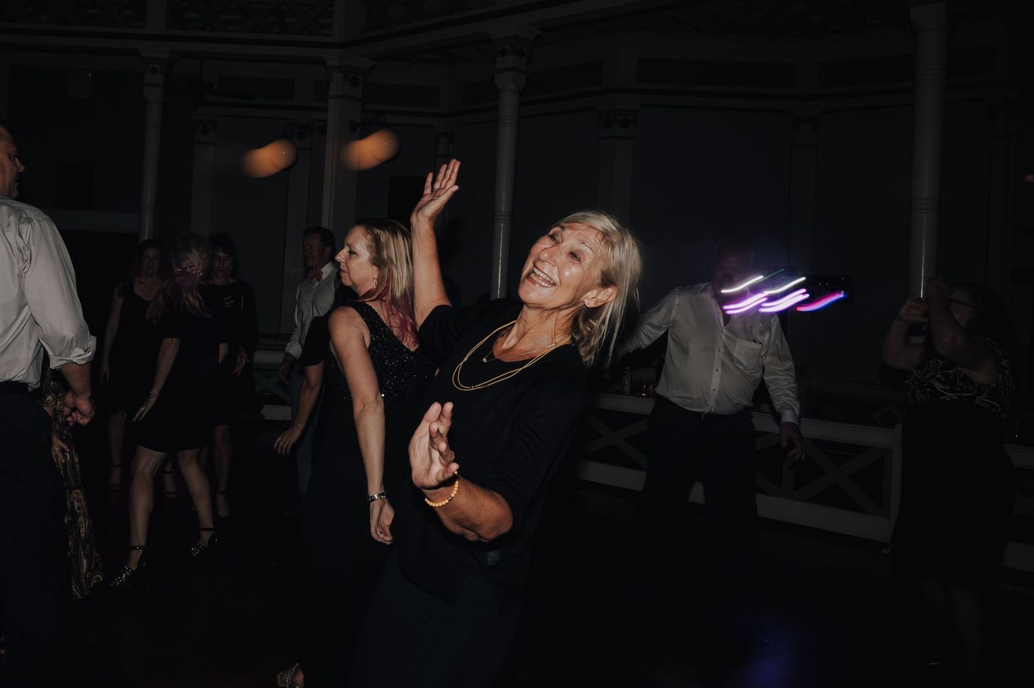 Party guests dancing under dim lighting with neon accents in the background.