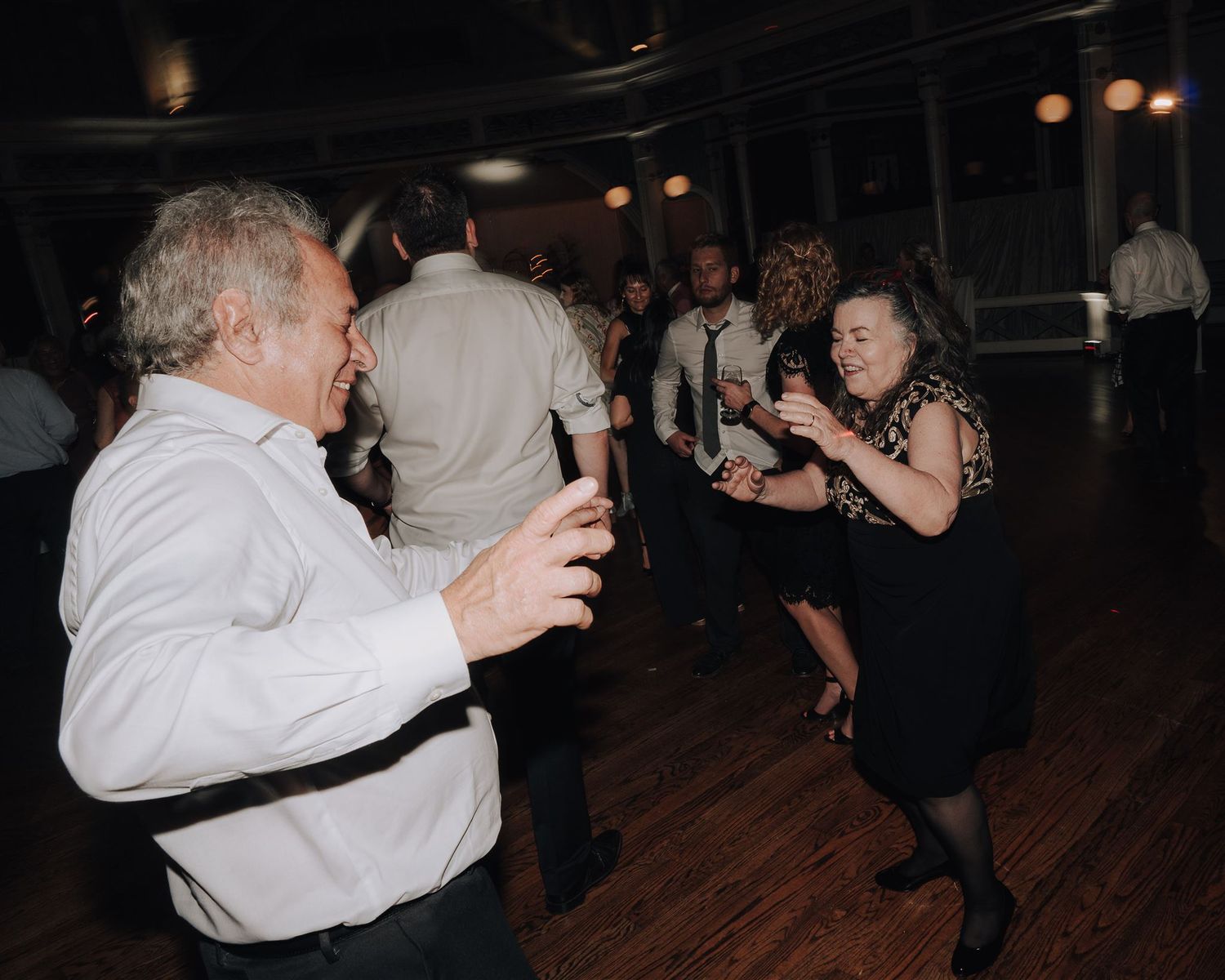 Party guests dance energetically on a hardwood floor during an evening celebration.