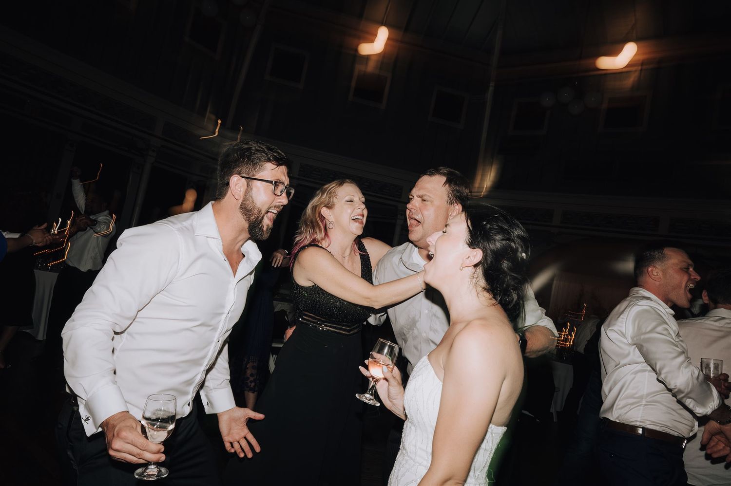 Wedding guests share a joyful moment while dancing at a reception celebration.