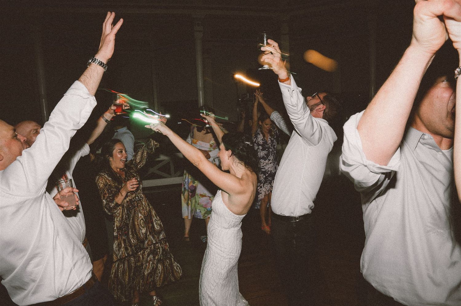 Party guests raise their hands in celebration while dancing at a reception.
