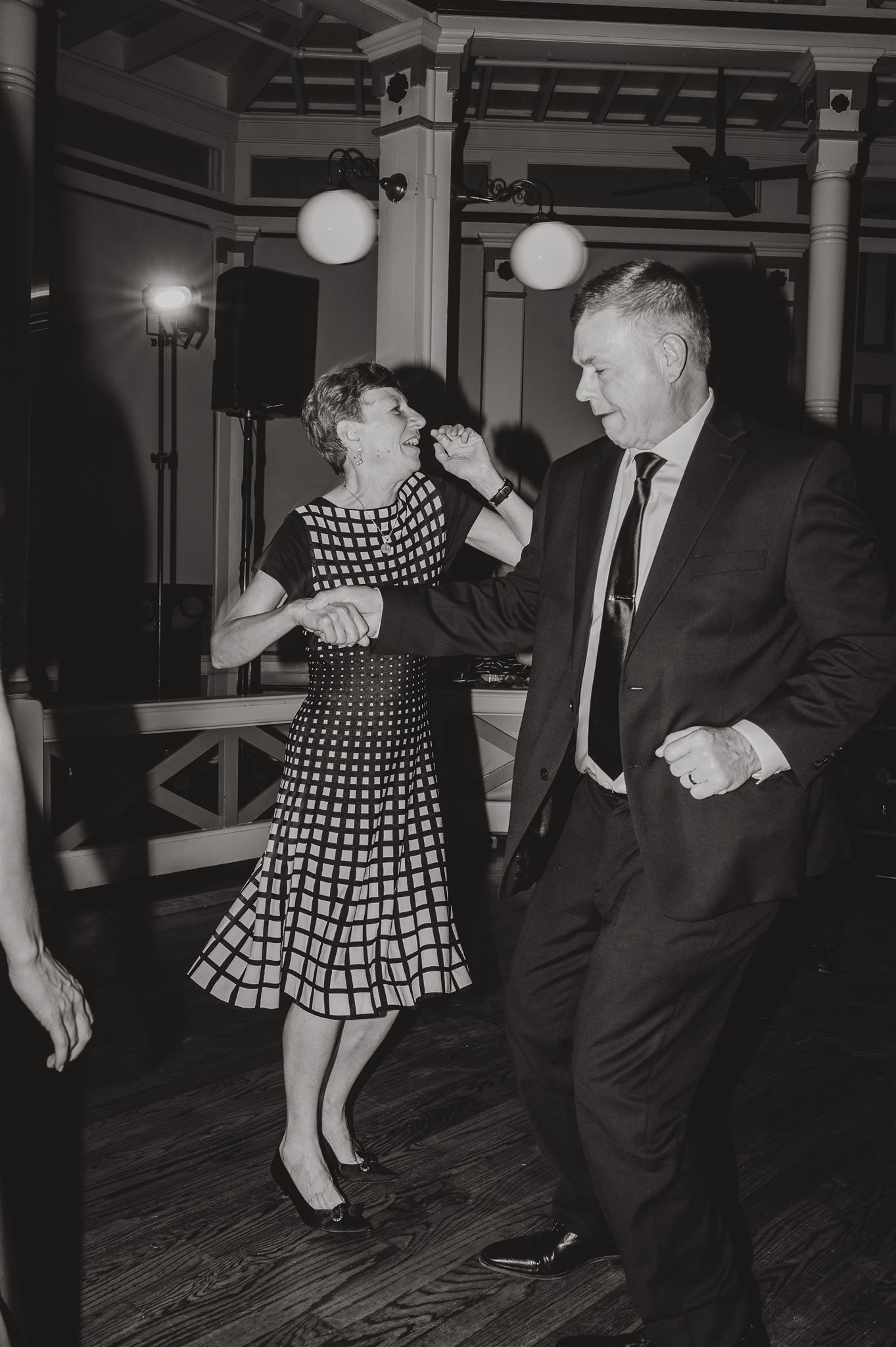 A couple dances energetically at a vintage-style celebration with globe lights overhead.
