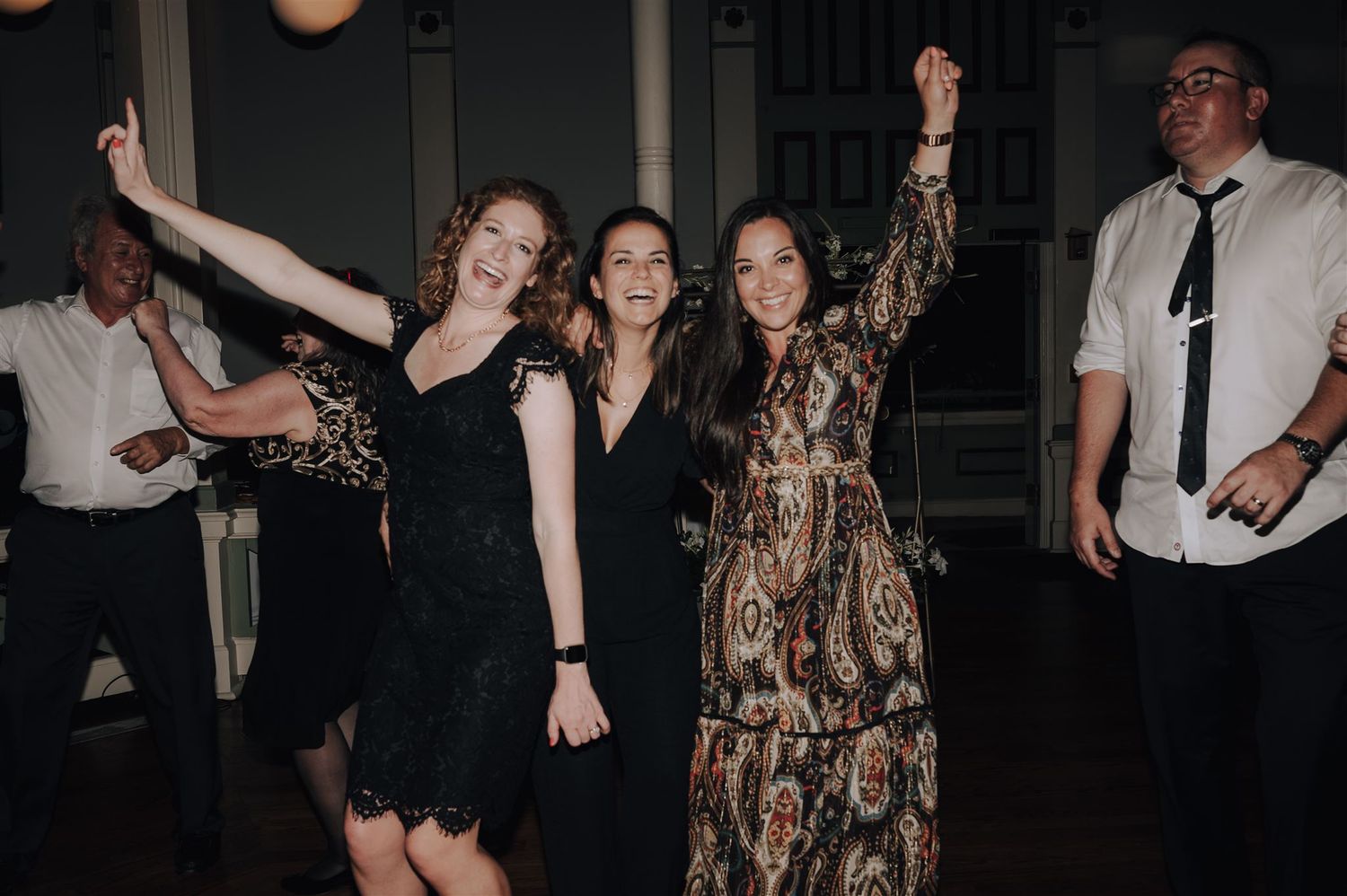 Group of party guests dancing with arms raised in celebration at an indoor venue.