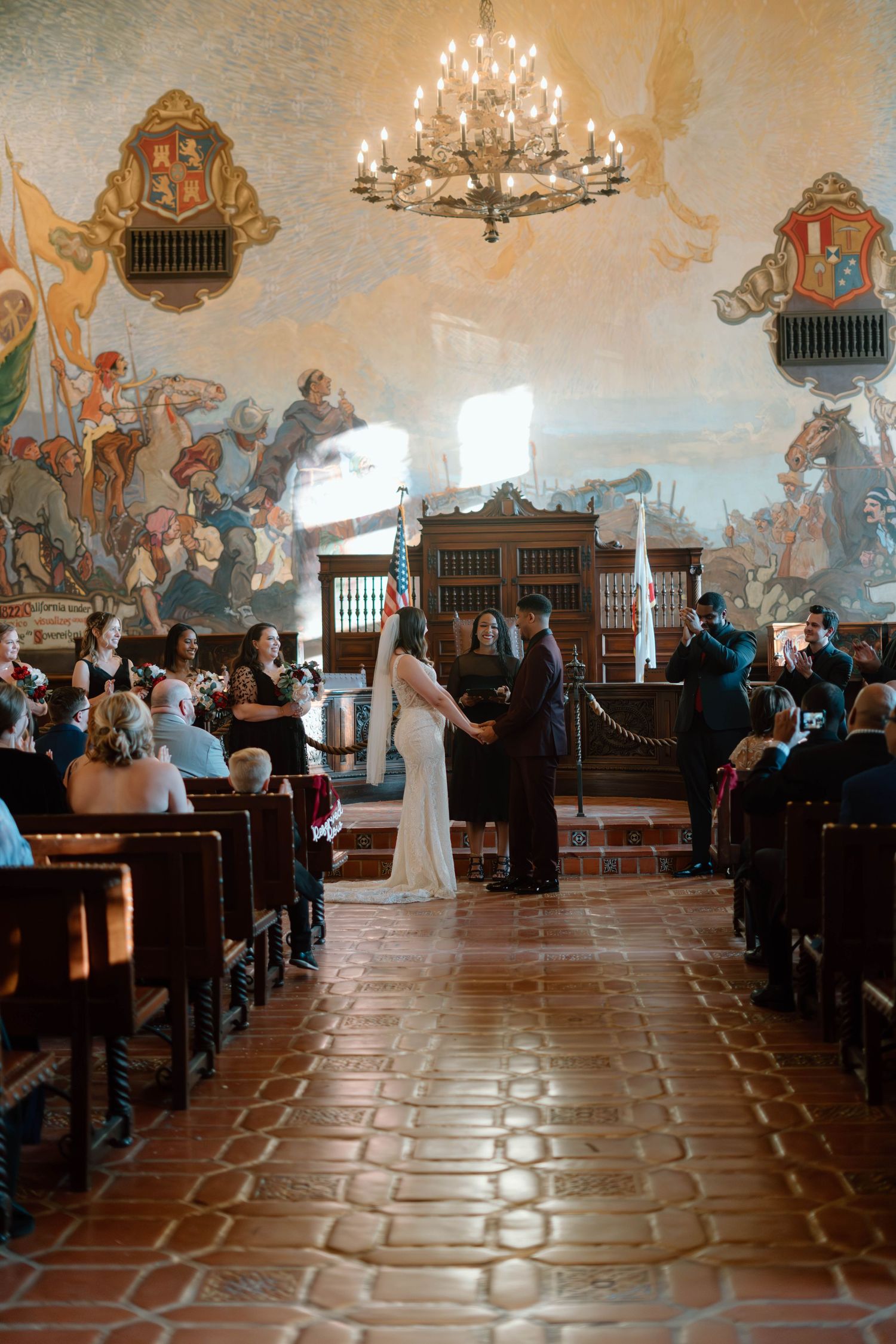 a bride and groom stand at the front of the room and hold hands during their ceremony at the Santa Barbara courthouse