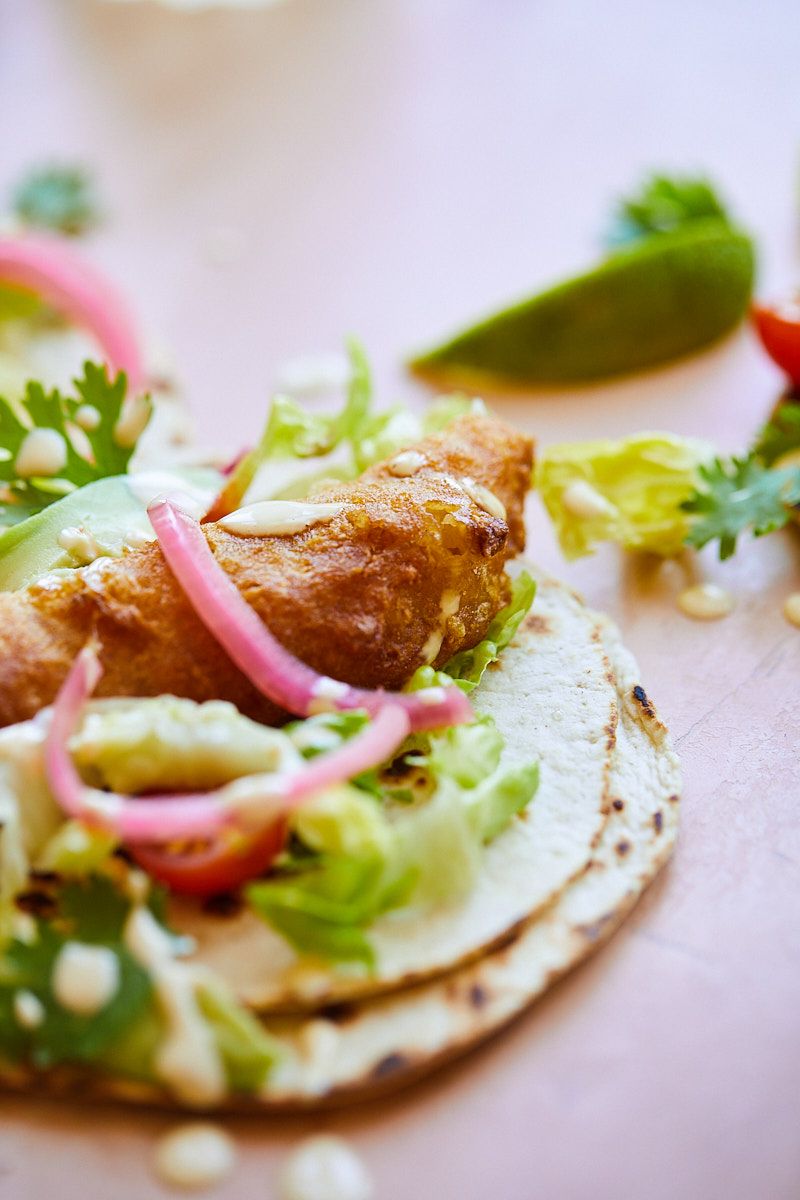 Close-up of fish taco with shredded lettuce and pickled red onions on corn tortilla.