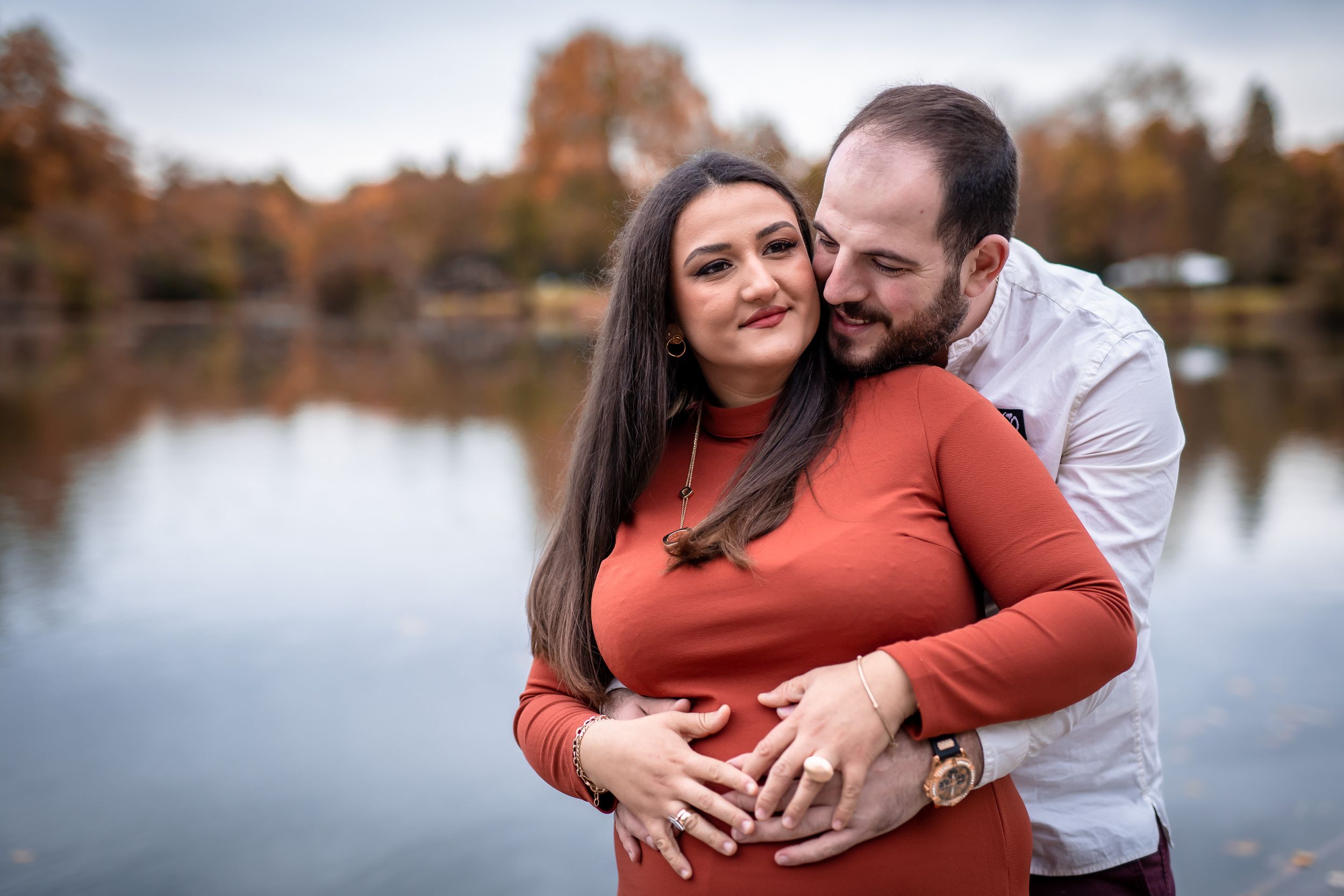 A romantic autumn lakeside moment with a couple embracing in front of reflective waters.