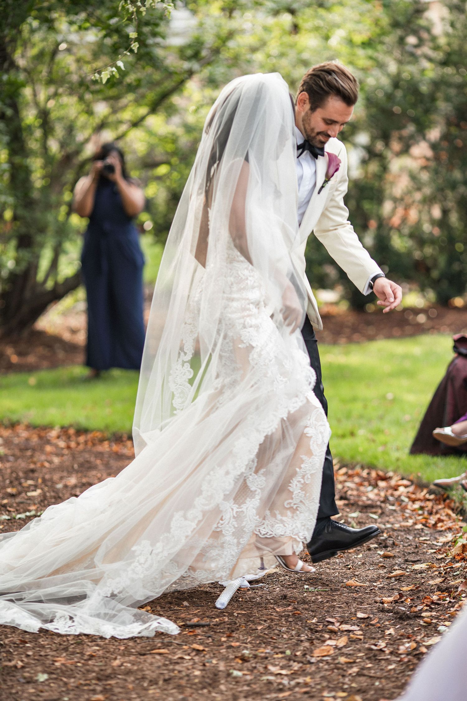 A outdoor wedding scene with a flowing lace wedding dress train on a woodland path.