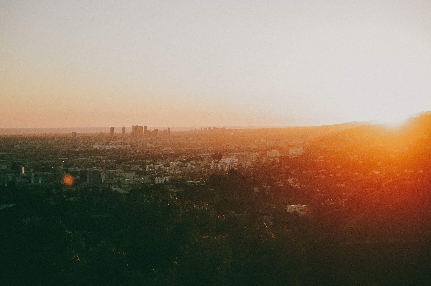 Sunset cityscape view with golden light casting over urban buildings and distant skyline in hazy atmosphere.