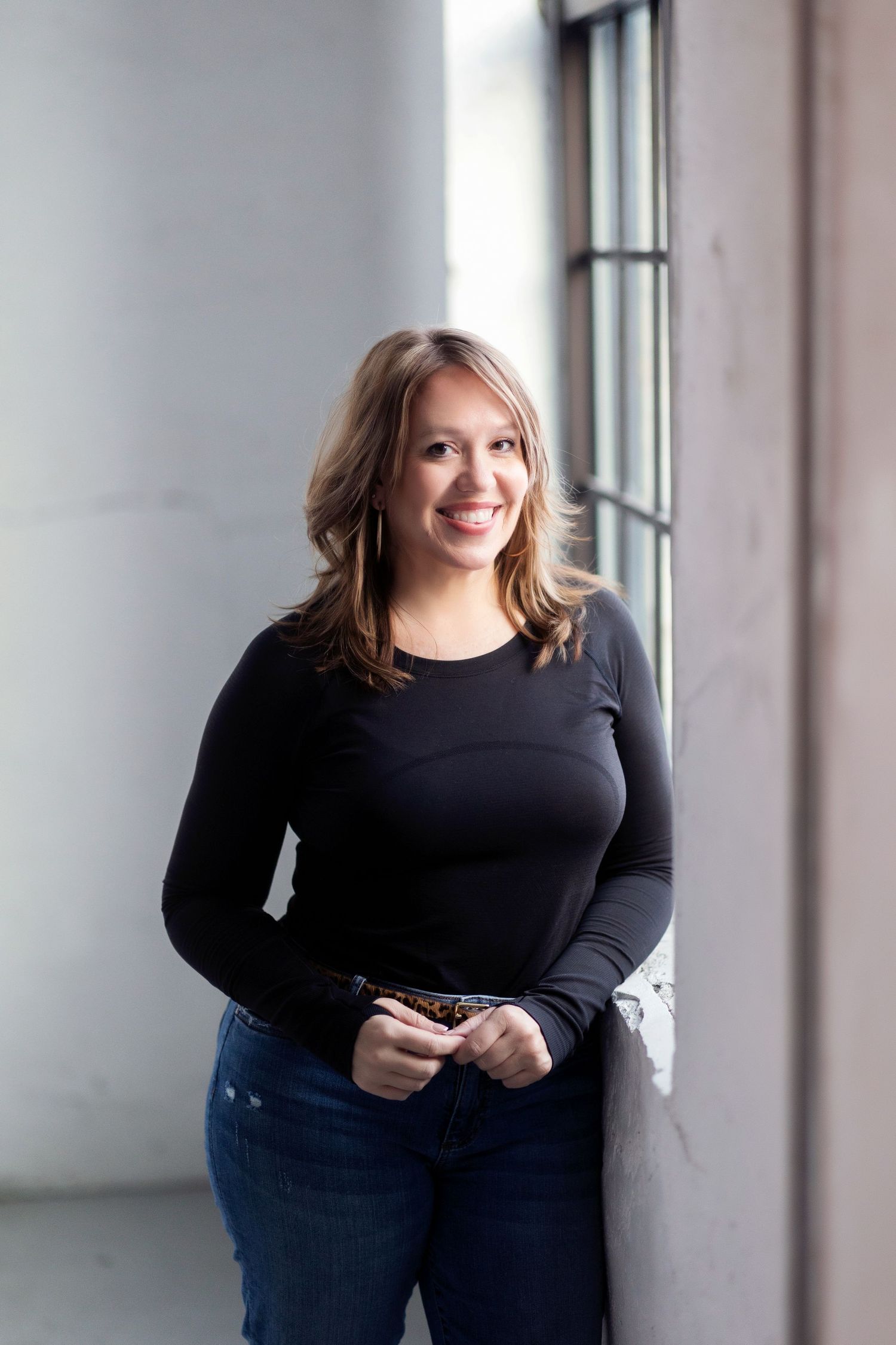 Professional studio portrait series in black outfit against a bright windowed background.
