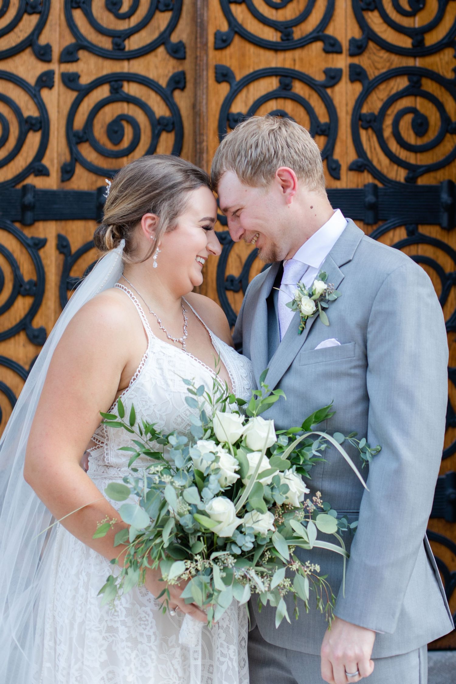Wedding couple shares intimate moment against decorative wooden backdrop with floral accents.