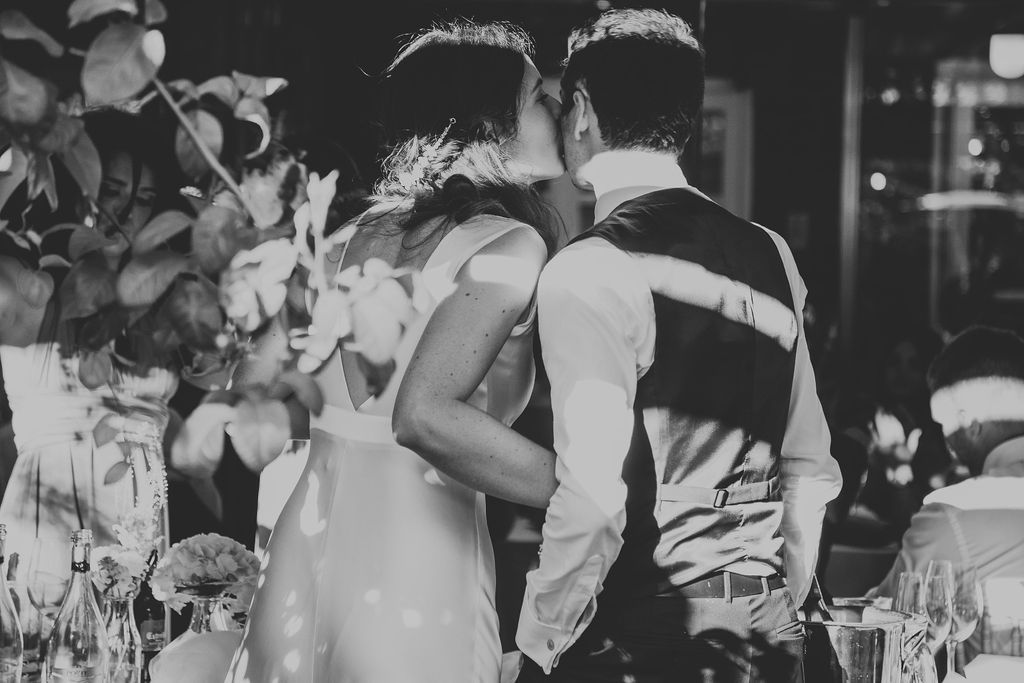 Black and white photo of couple embracing at wedding reception with floral decorations in foreground.