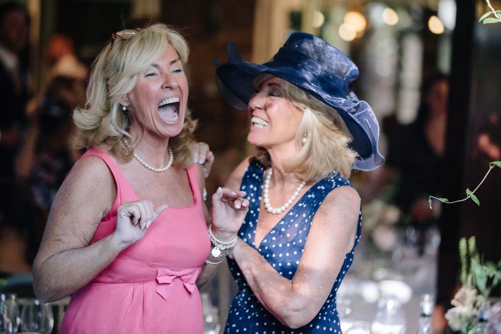Two guests in bright dresses laughing at a wedding