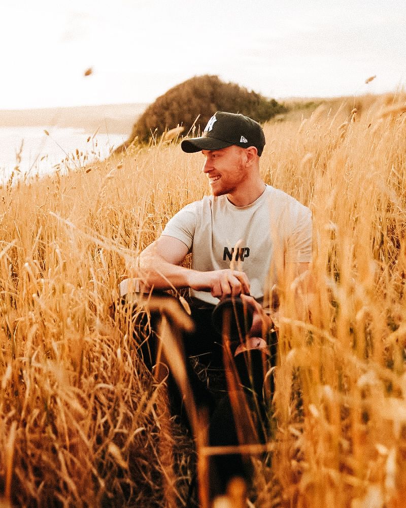 Person standing in golden wheat field at sunset wearing a baseball cap.