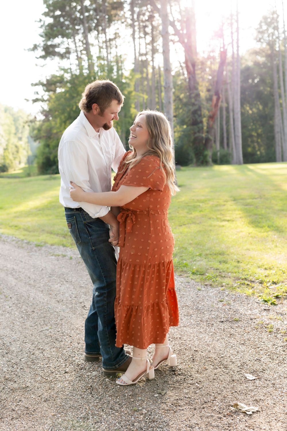 A romantic moment between a couple on a gravel path surrounded by green trees at sunset.