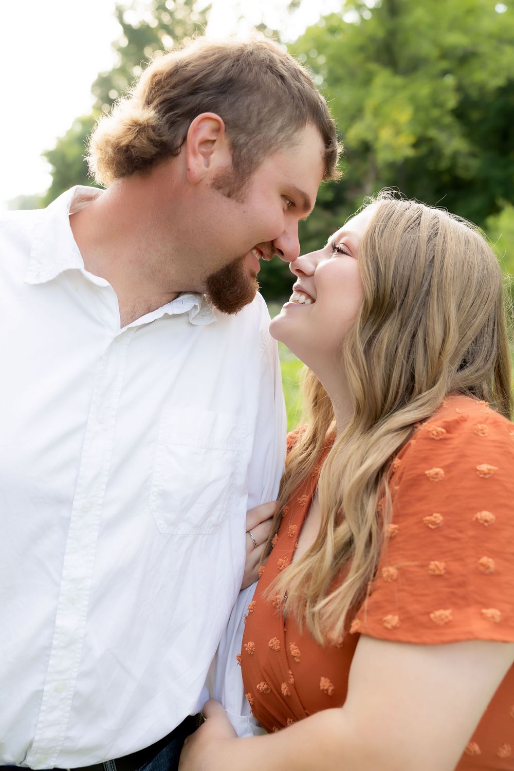 A joyful intimate moment shared between a couple in casual attire against a sunlit natural backdrop.