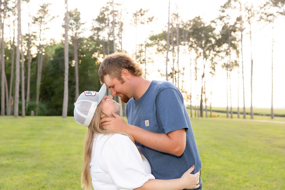 A romantic couple embraces in an outdoor setting with tall pine trees at sunset.