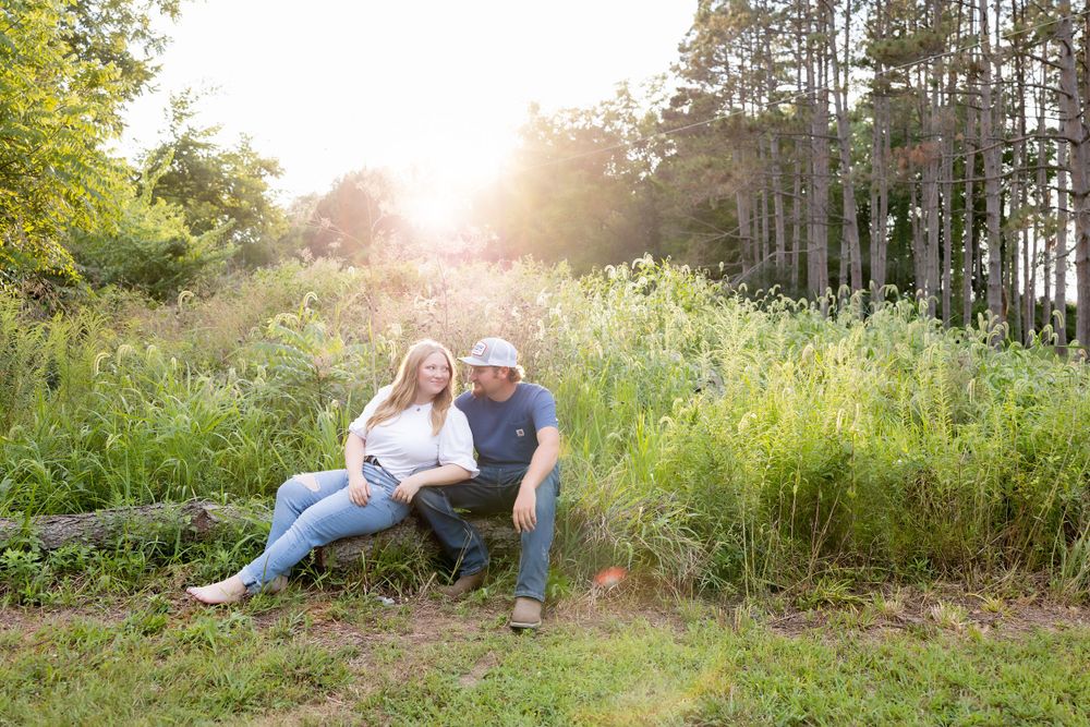A couple relaxes together on a grassy hillside during golden hour with pine trees in the background.