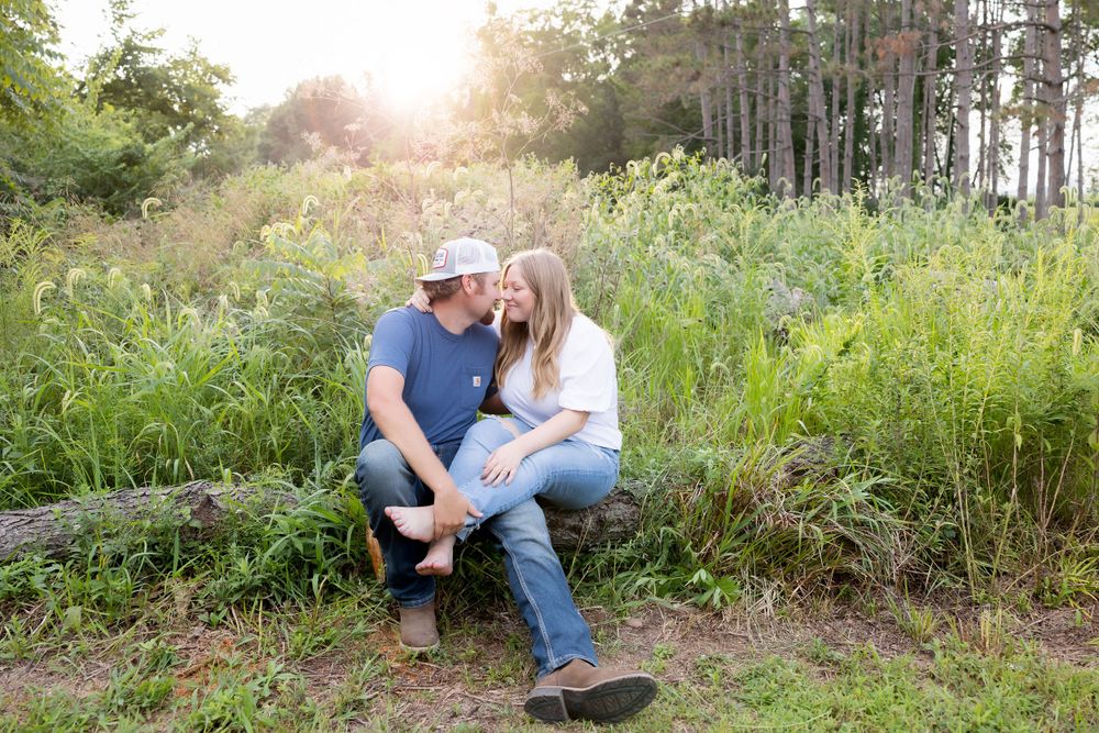 A couple sharing a tender moment while sitting among tall grass and pine trees at sunset.