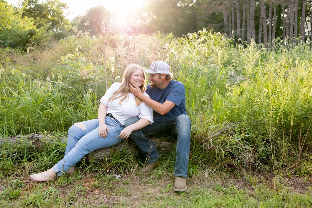 A couple shares a romantic moment while sitting on a grassy hill during sunset.