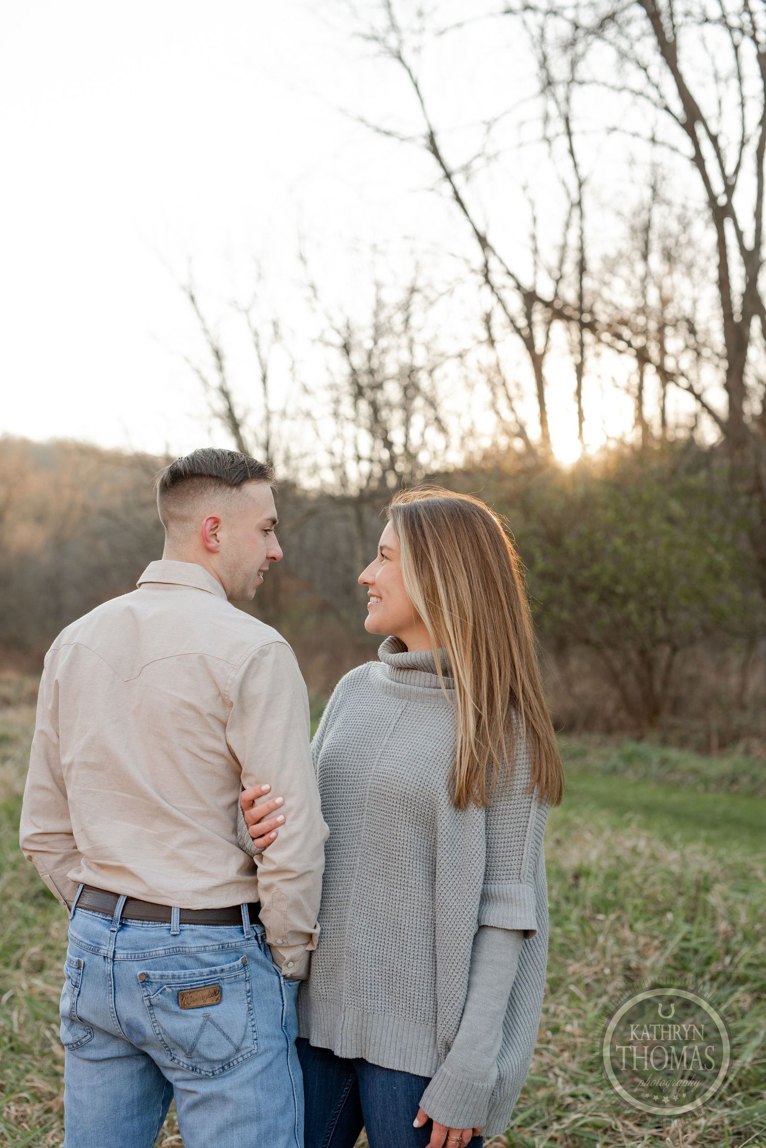 A couple shares a candid moment together in casual attire against an autumn landscape.