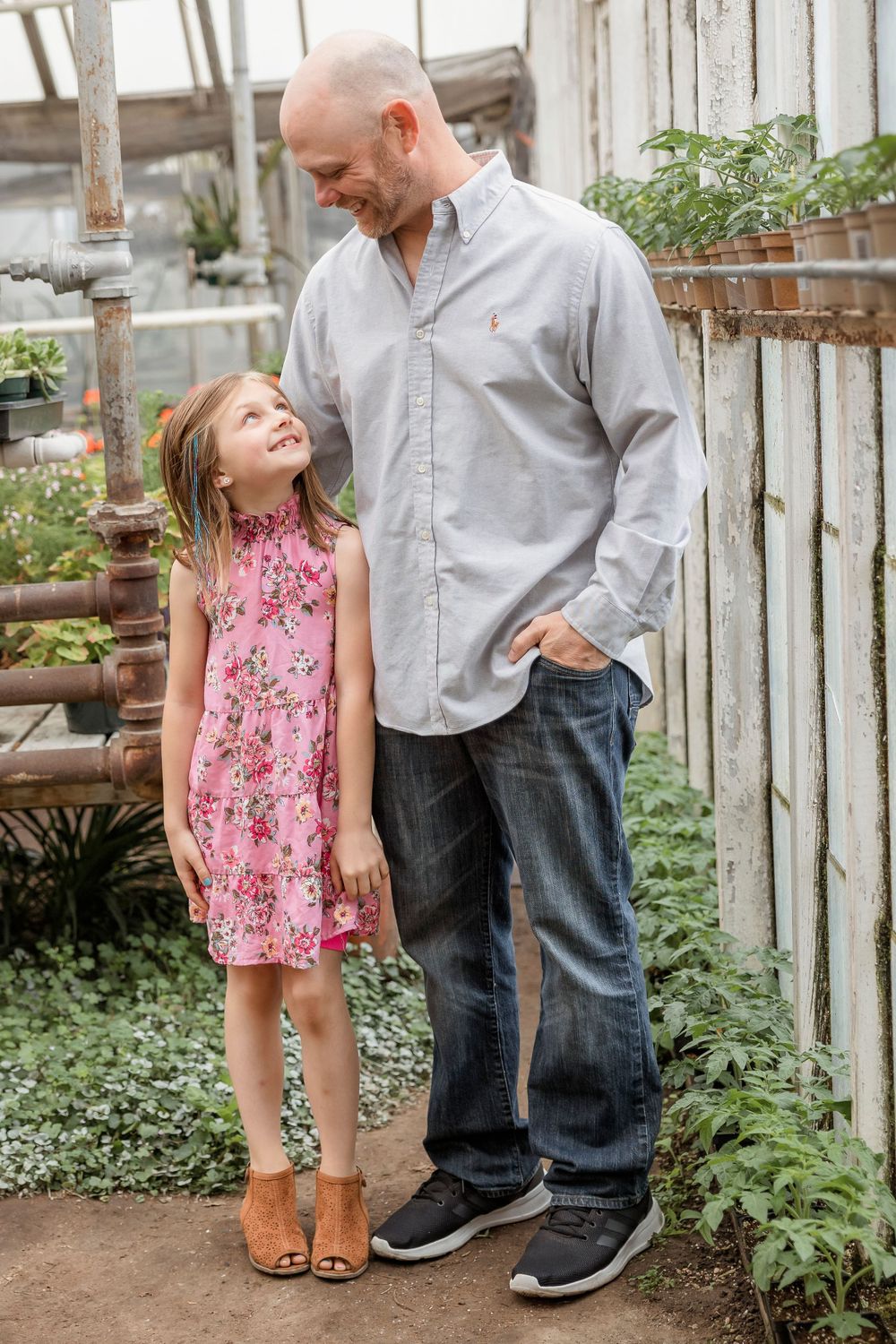 Sweet interaction between parent and child in floral dress inside rustic greenhouse setting.