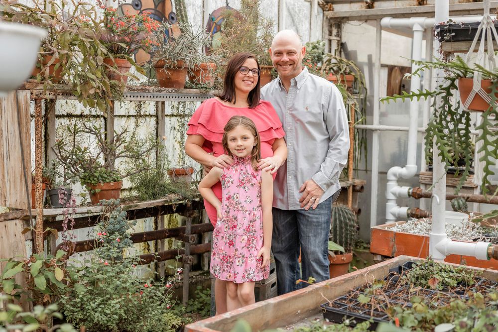 A family stands together among potted plants in a greenhouse environment.