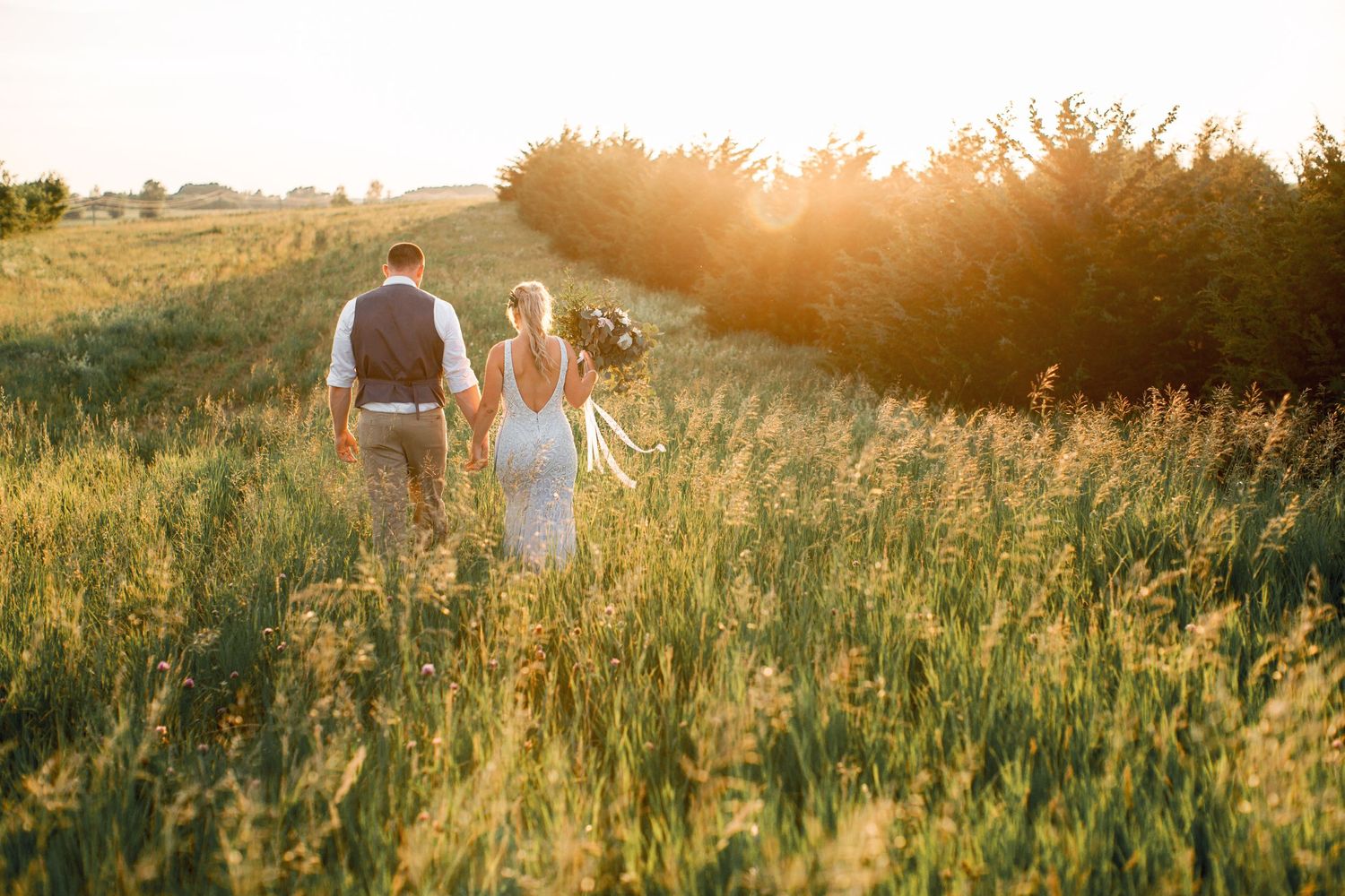 Bride and groom walking through a Minnesota field at sunset. Wedding photography by Laura Leigh Images