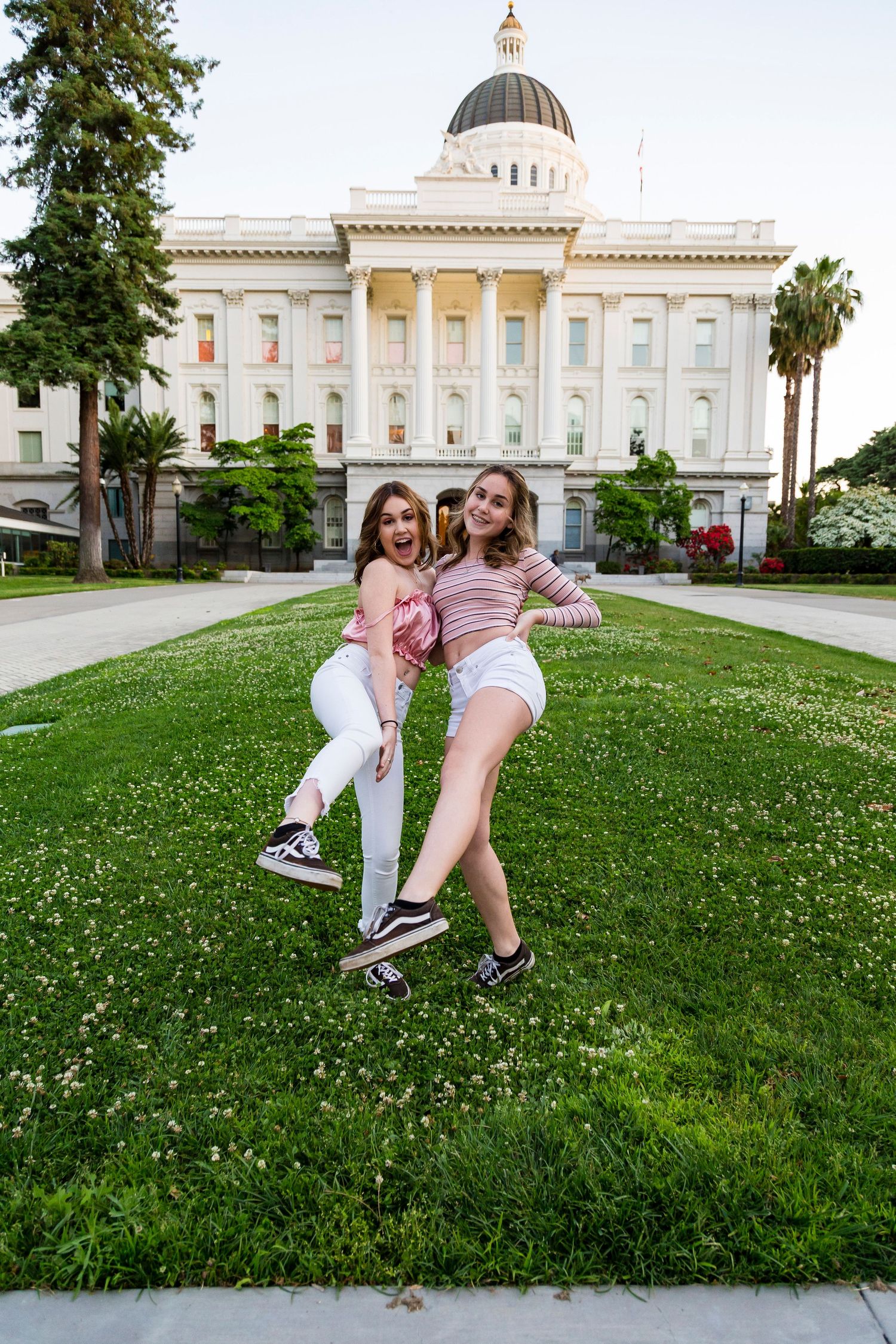 sisters kicking their outside legs toward the camera while on the grass outside the capital building