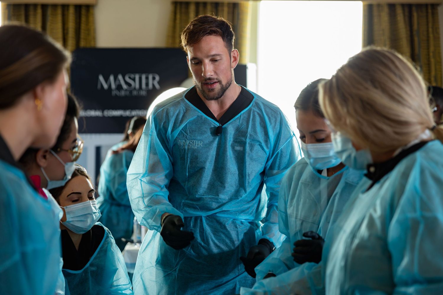 Medical professionals in teal scrubs and protective gear gather together during a discussion in a clinical setting.