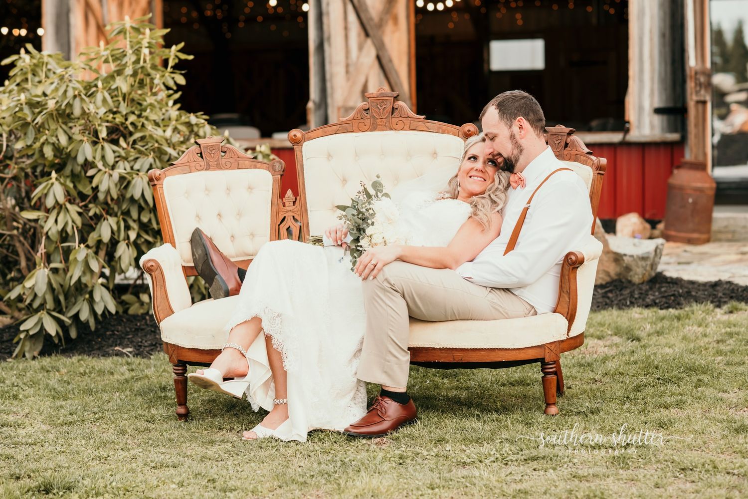 A couple relaxes together on an elegant vintage settee outdoors during a romantic garden wedding celebration.