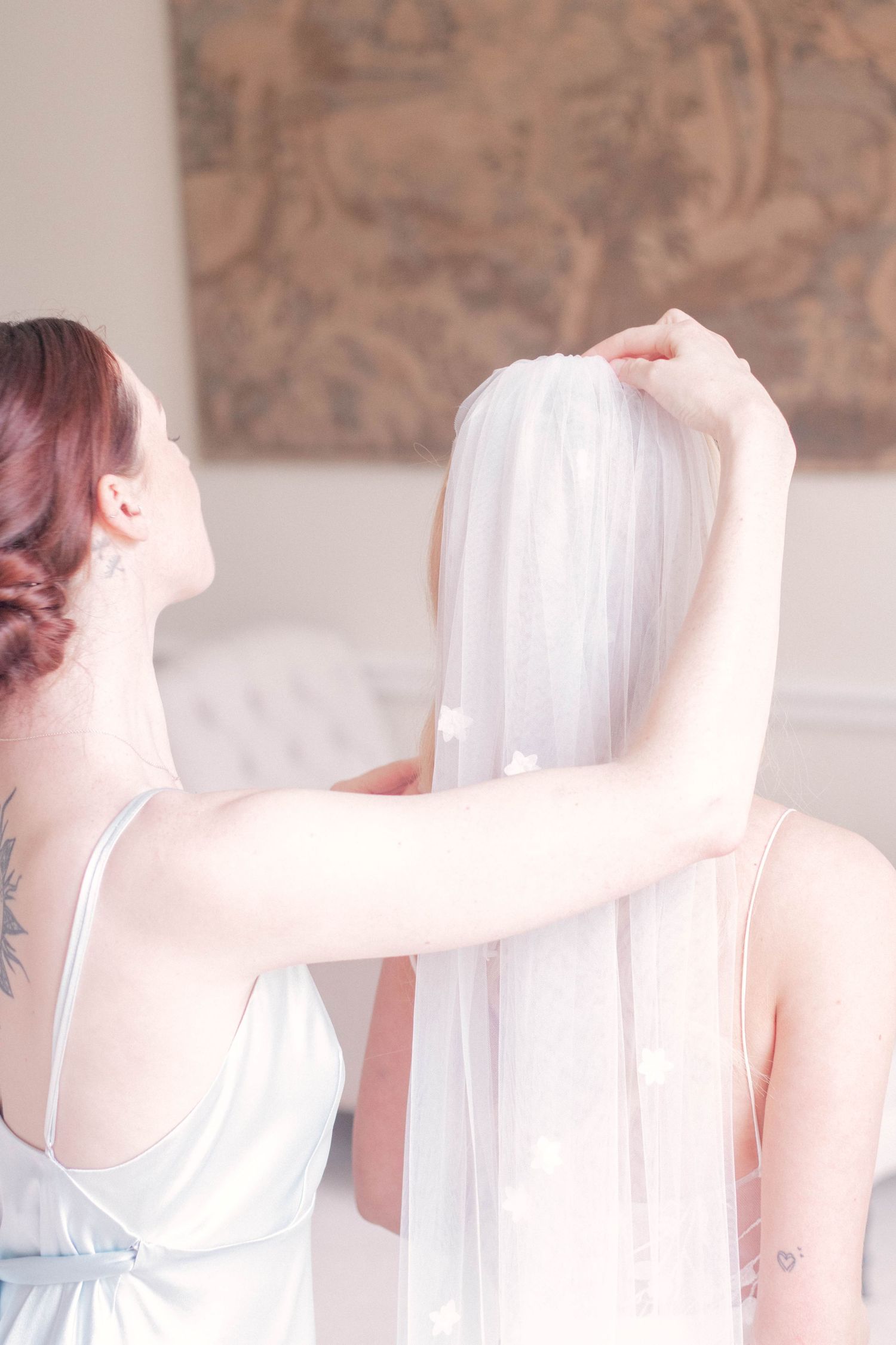 Bridesmaid adjusting white wedding veil in elegant interior setting.