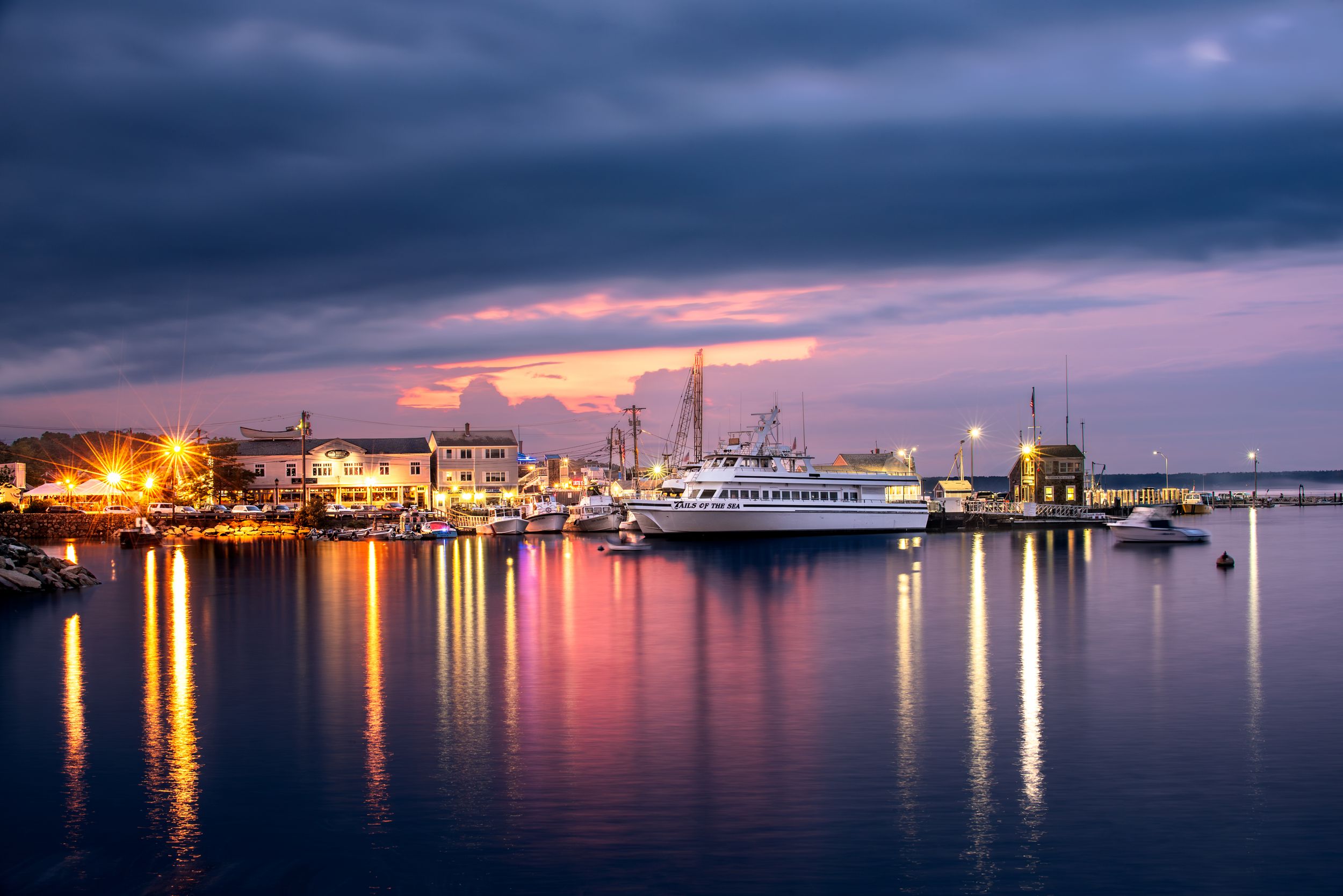 Harbor at twilight with boats and city lights reflecting on purple-tinted water.