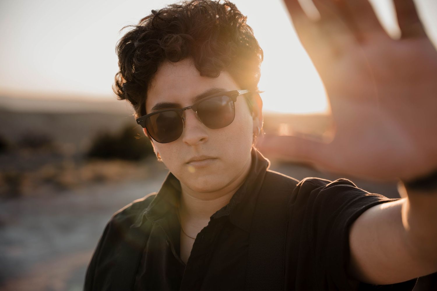 Person wearing sunglasses sits against warm sunset backdrop in desert landscape.