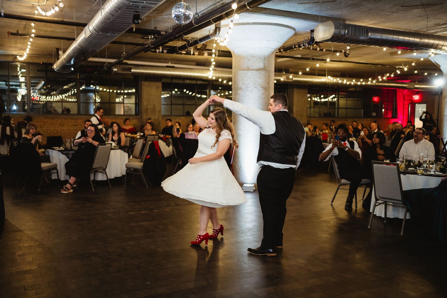 A couple performs a dance spin during their wedding reception in an industrial-style venue.