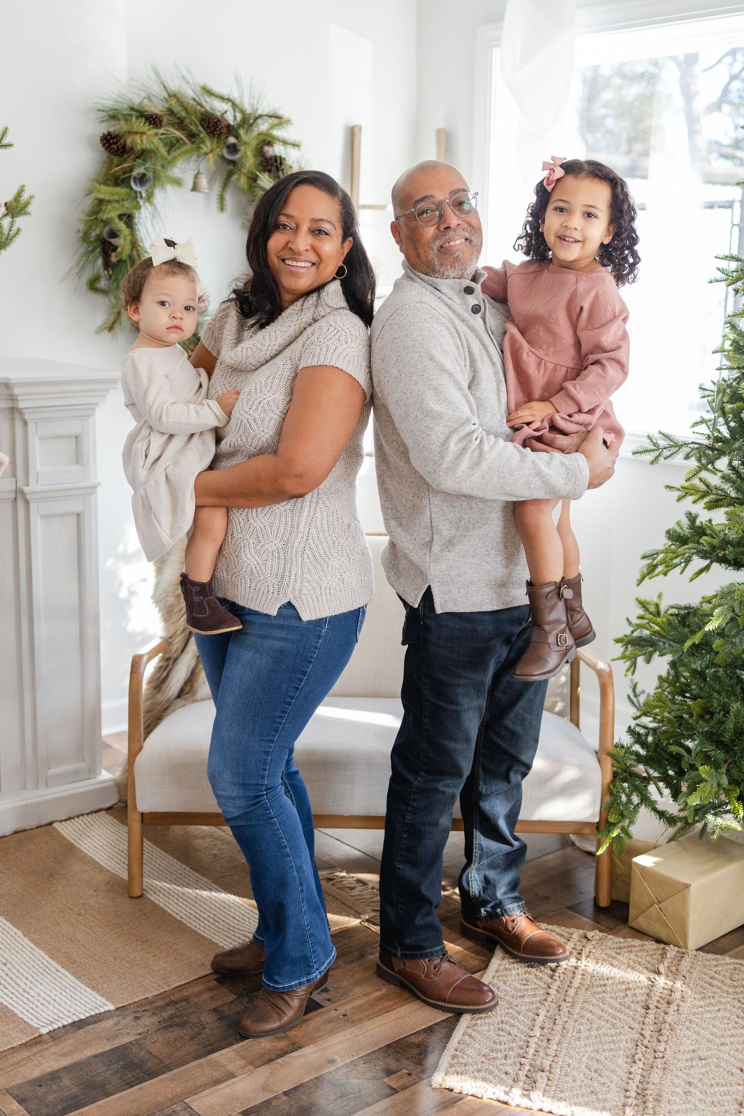Couple holding children pose in front of Christmas decorations in cozy living room setting.