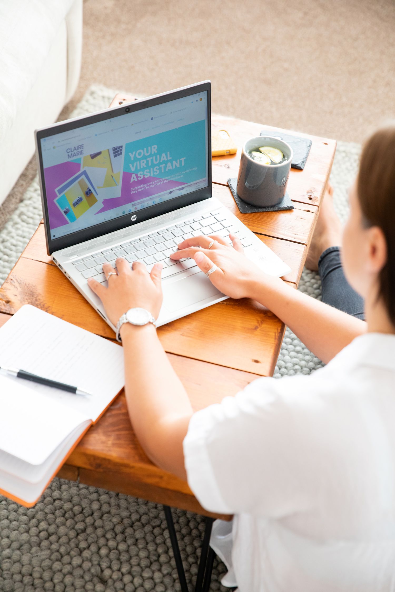 A laptop displays a colorful website design while someone works at a wooden desk during business branding photoshoot.