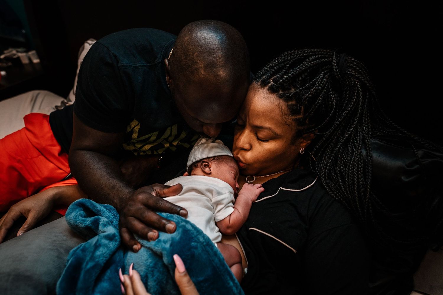 Black Couple Kissing Newborn Baby Laying On Woman's Chest