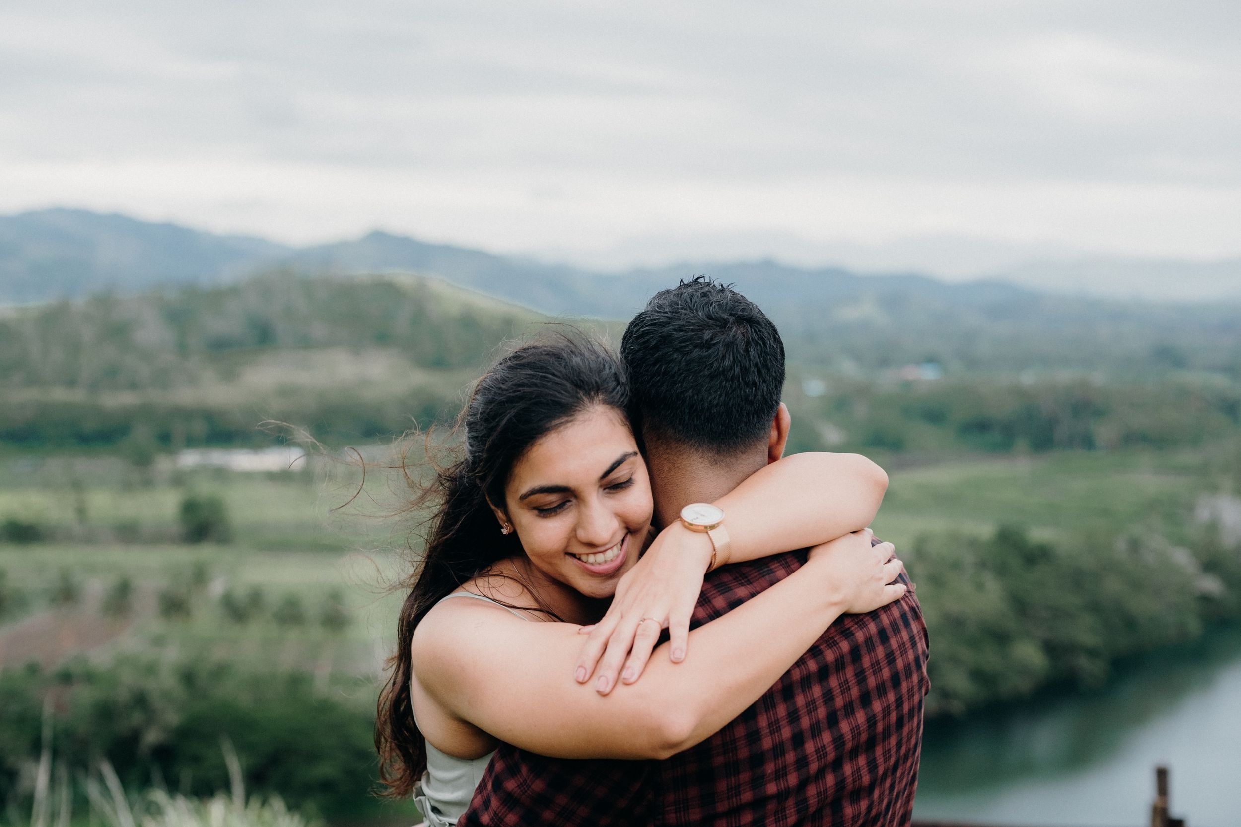 A tender embrace shared on a hilltop with a scenic river valley in the background.