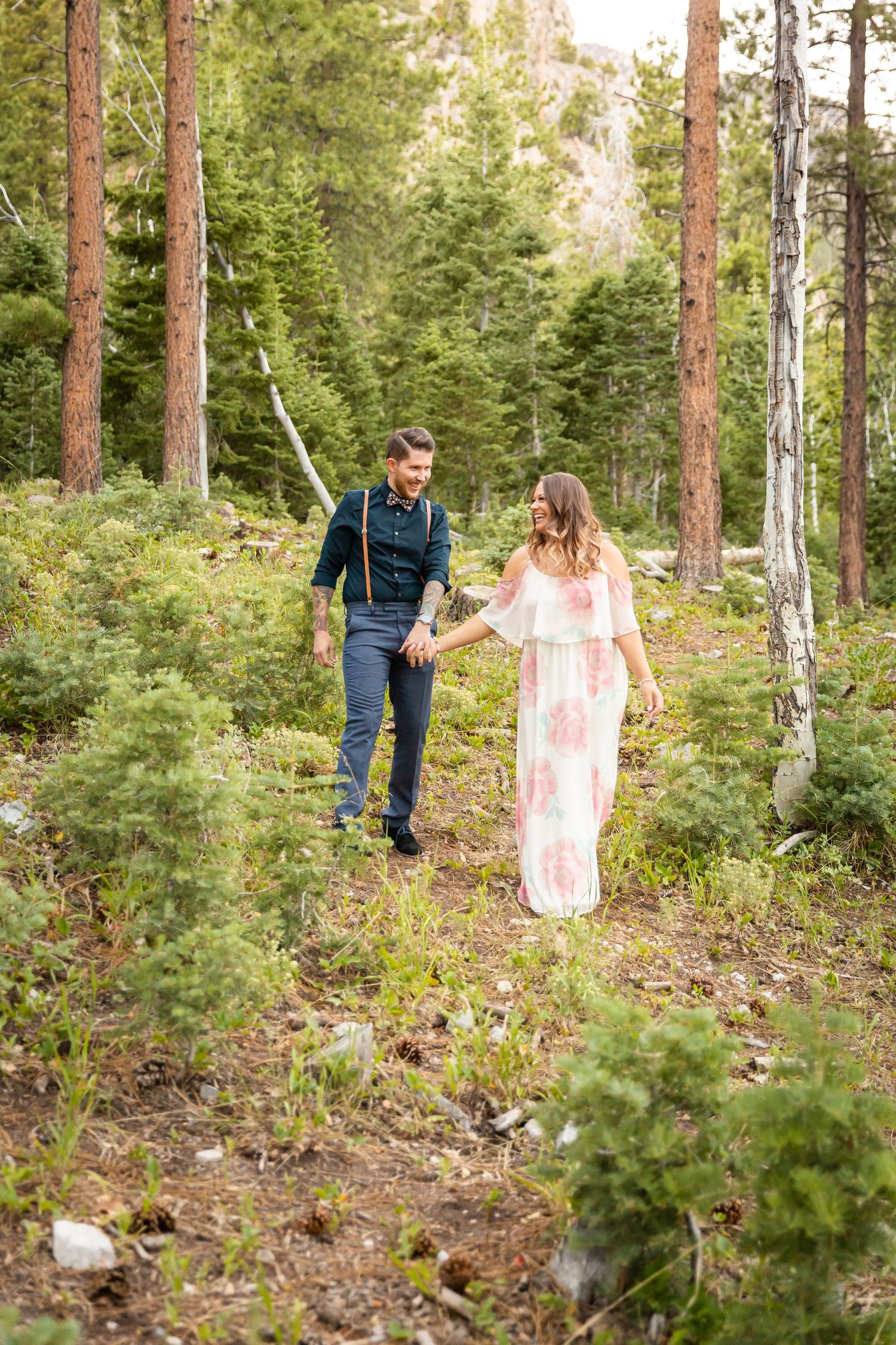 A couple explores a scenic mountain trail together among towering pine trees.