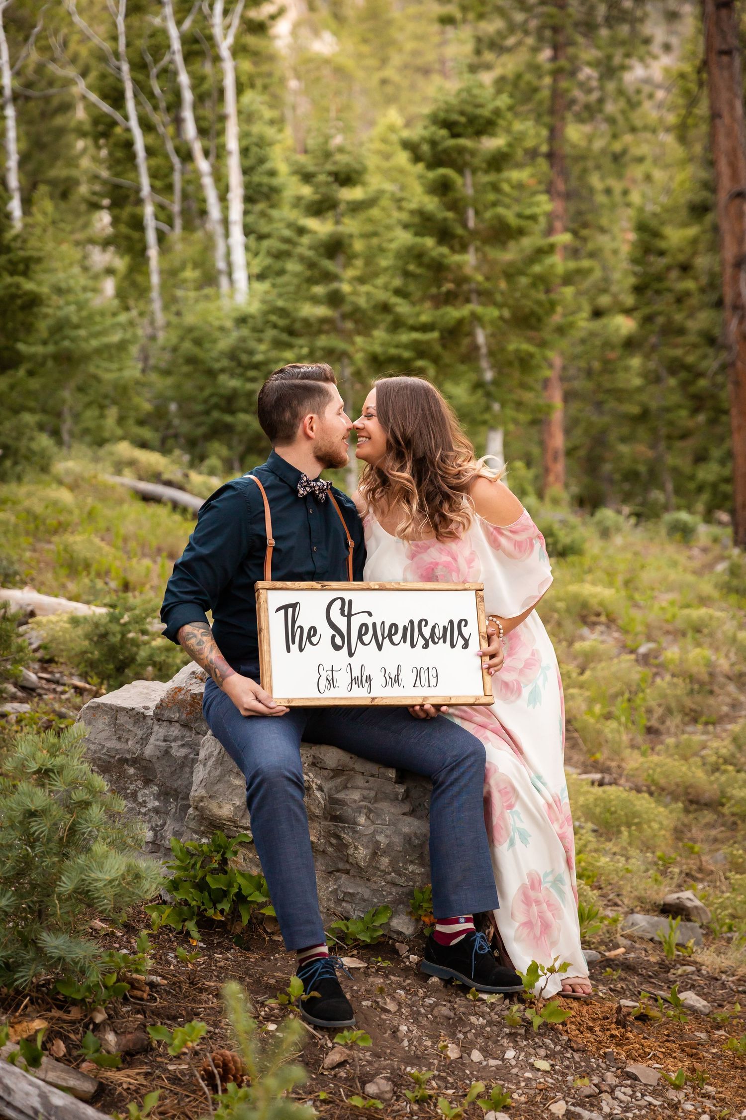 Intimate moment captured between couple holding wedding sign in forest setting.