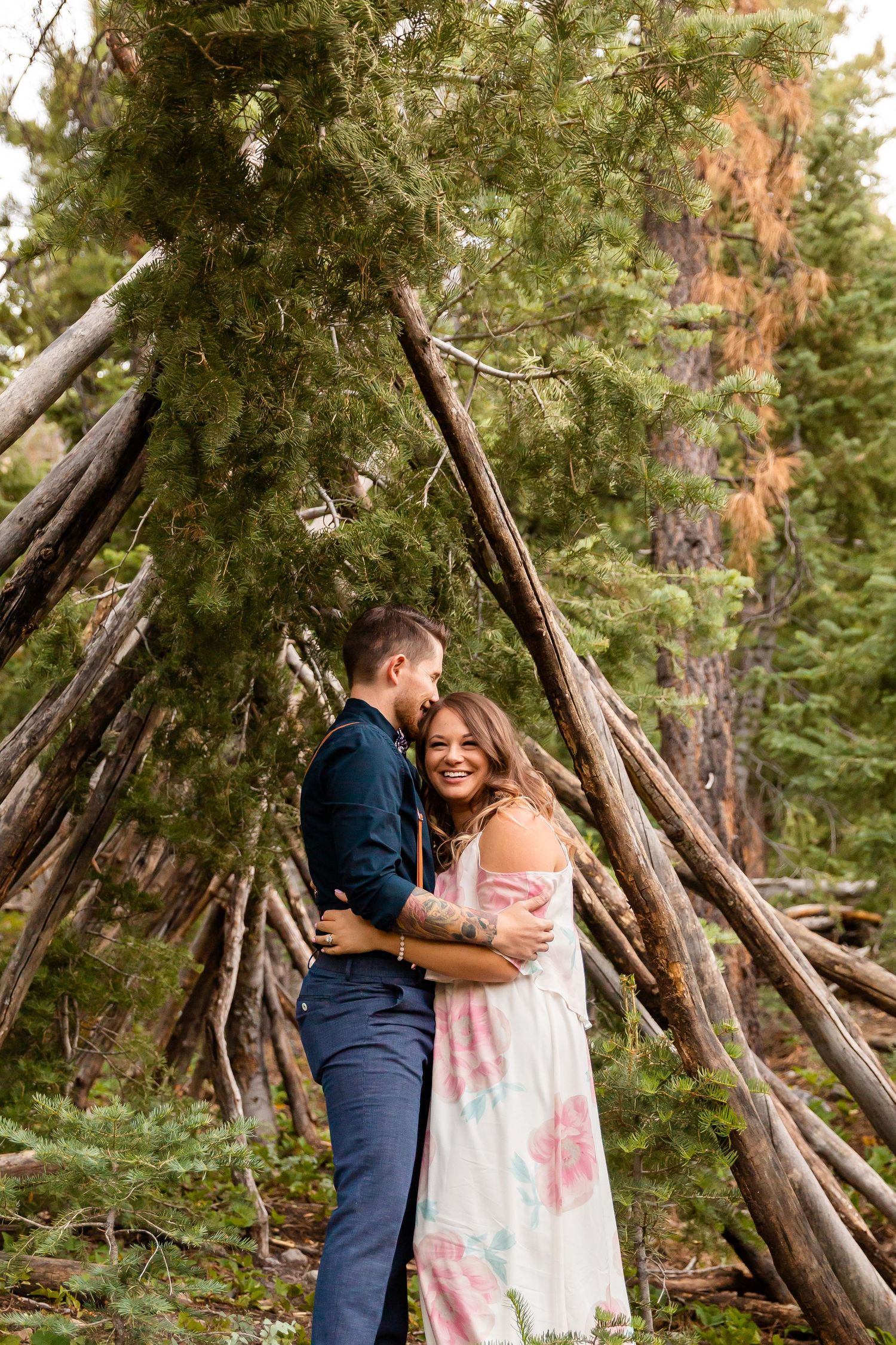 Couple sharing intimate moment by wooden teepee structure in forest setting.